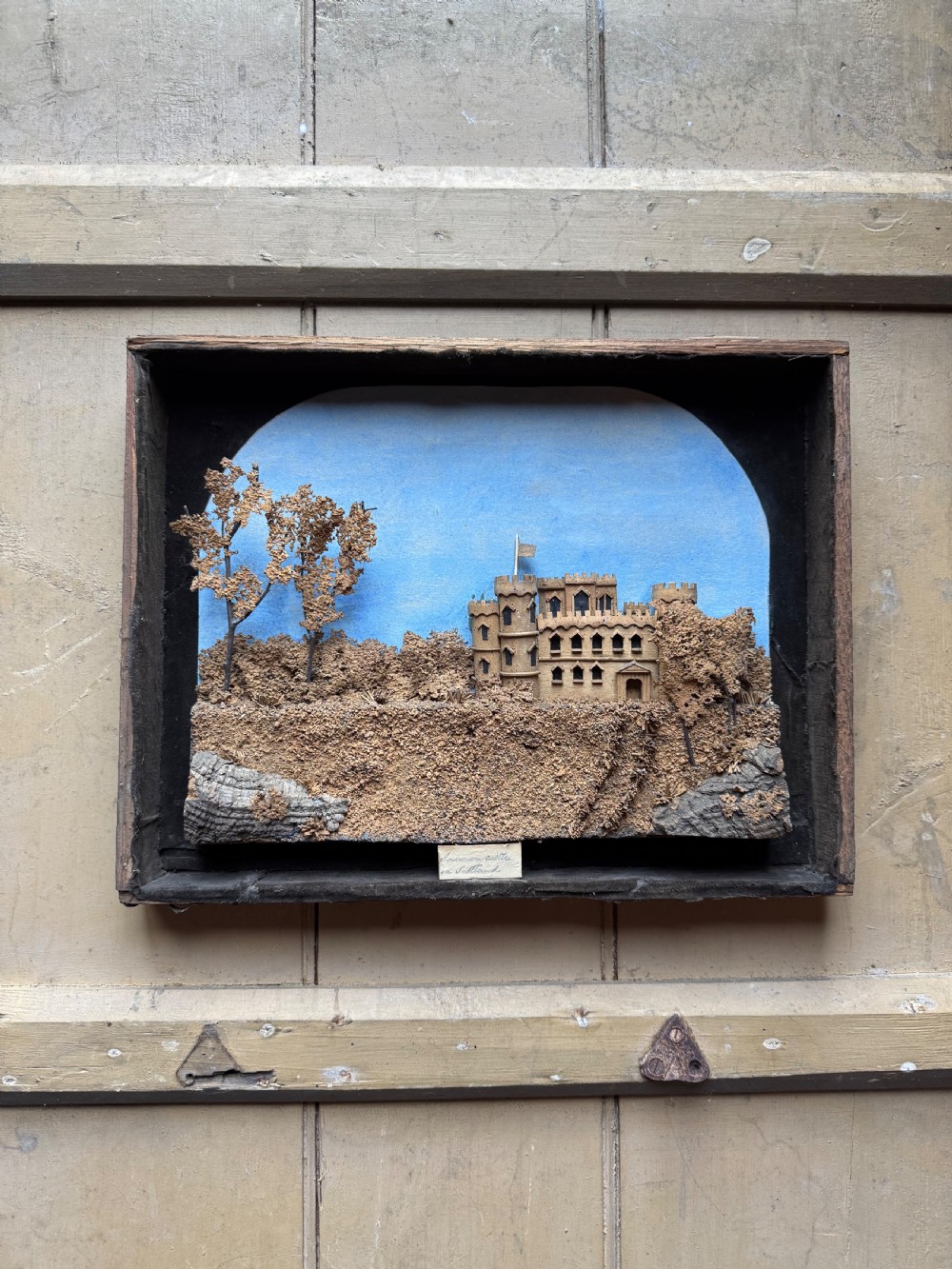 A framed nineteenth-century three-dimensional cork diorama depicting a castle on a hill against a painted light blue backdrop inside a glazed moulded frame. View V