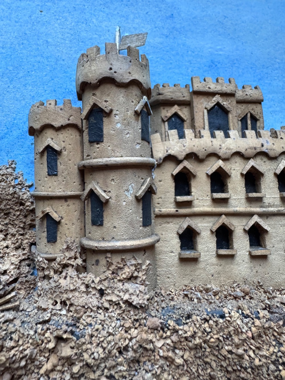 A framed nineteenth-century three-dimensional cork diorama depicting a castle on a hill against a painted light blue backdrop inside a glazed moulded frame. View VII
