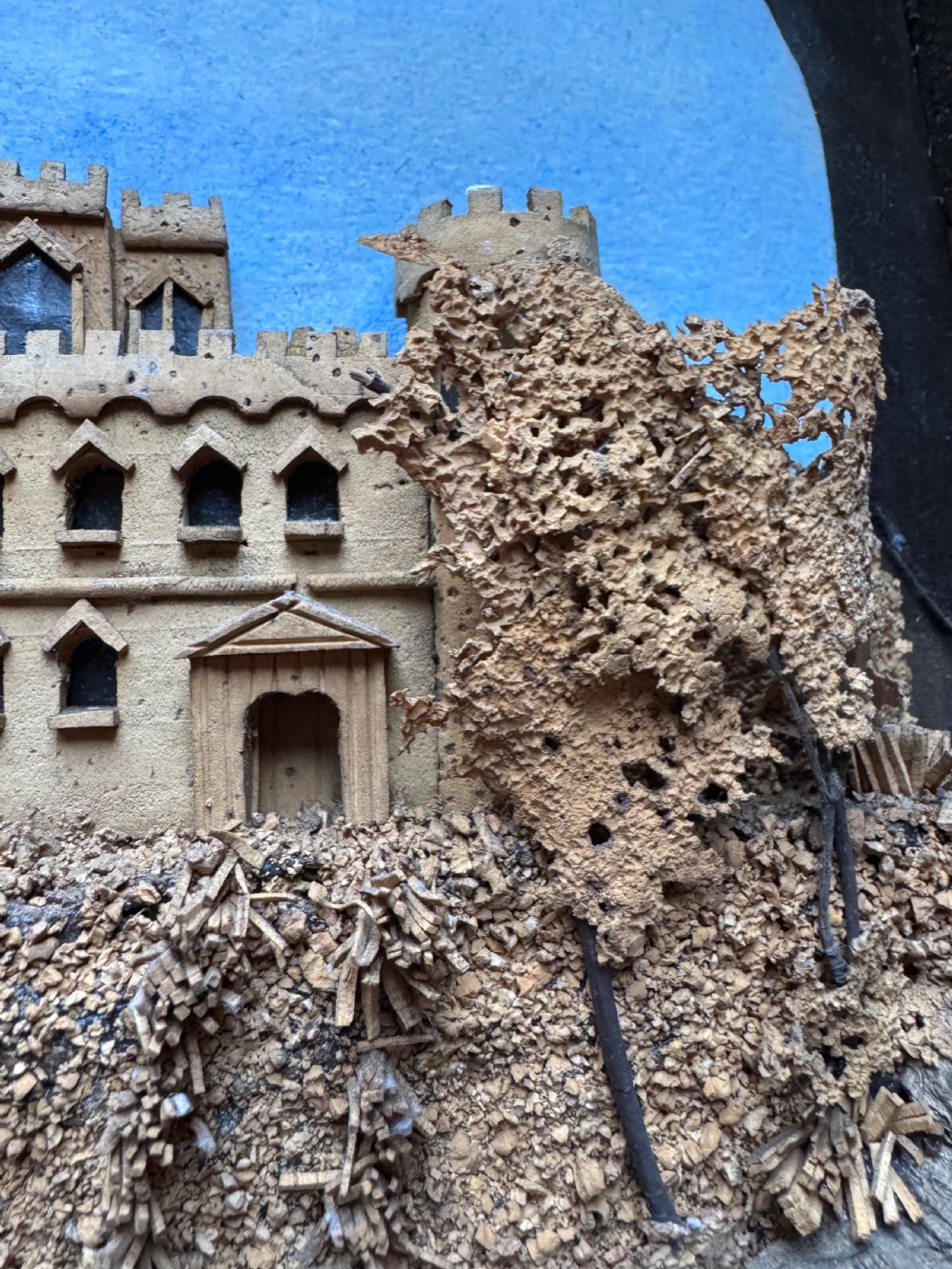 A framed nineteenth-century three-dimensional cork diorama depicting a castle on a hill against a painted light blue backdrop inside a glazed moulded frame. View VIII