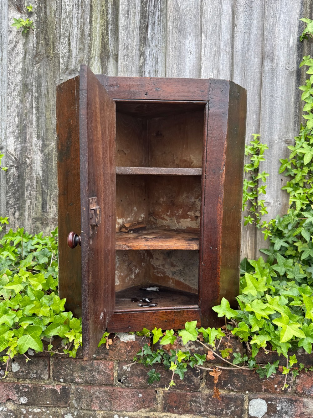 An antique dark oak provincial cupboard featuring canted sides, a single panelled door, a wooden knob, and an iron keyhole escutcheon. View VIII