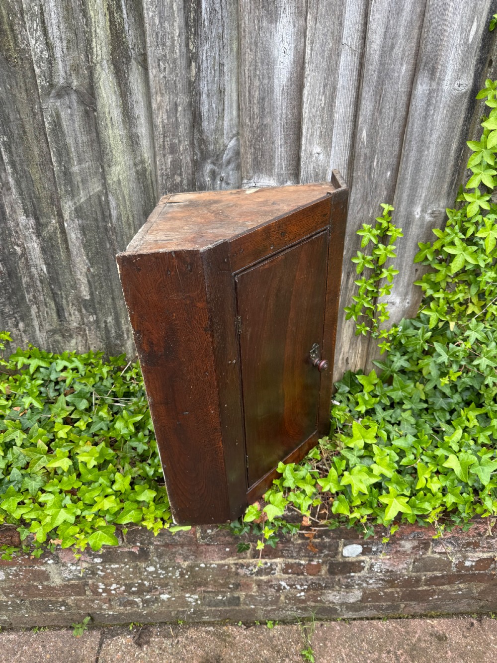 An antique dark oak provincial cupboard featuring canted sides, a single panelled door, a wooden knob, and an iron keyhole escutcheon. View XI