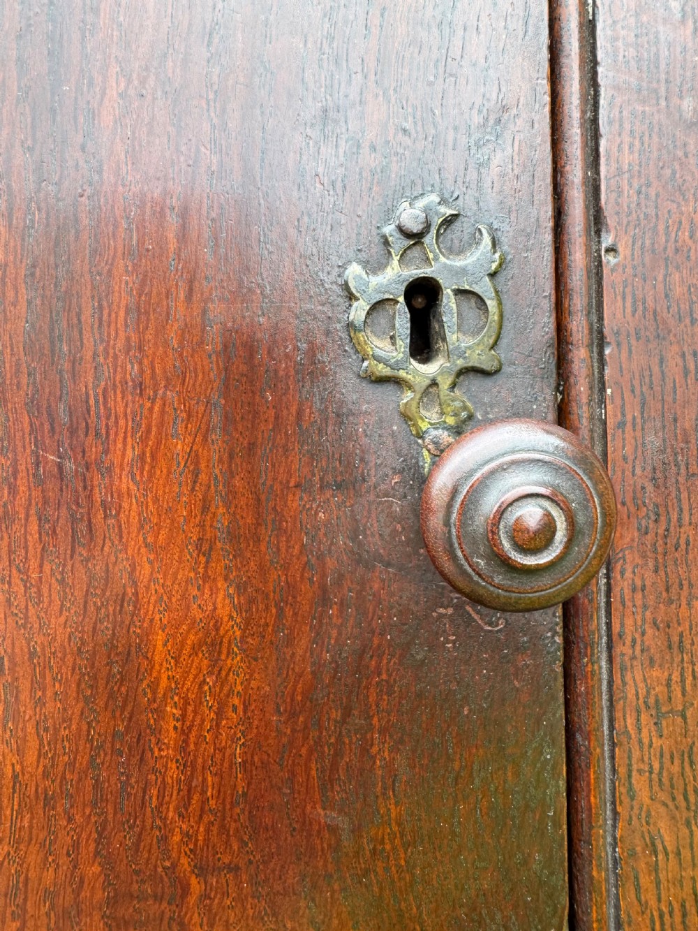 An antique dark oak provincial cupboard featuring canted sides, a single panelled door, a wooden knob, and an iron keyhole escutcheon. View XIII