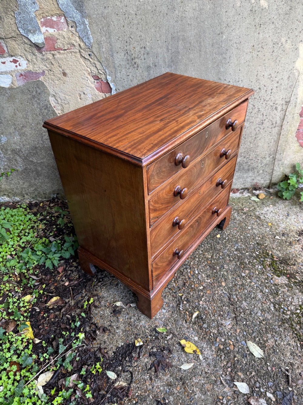 A Georgian mahogany chest featuring four graduated drawers with turned wooden knobs, keyhole escutcheons, and classic bracket feet. View XVI