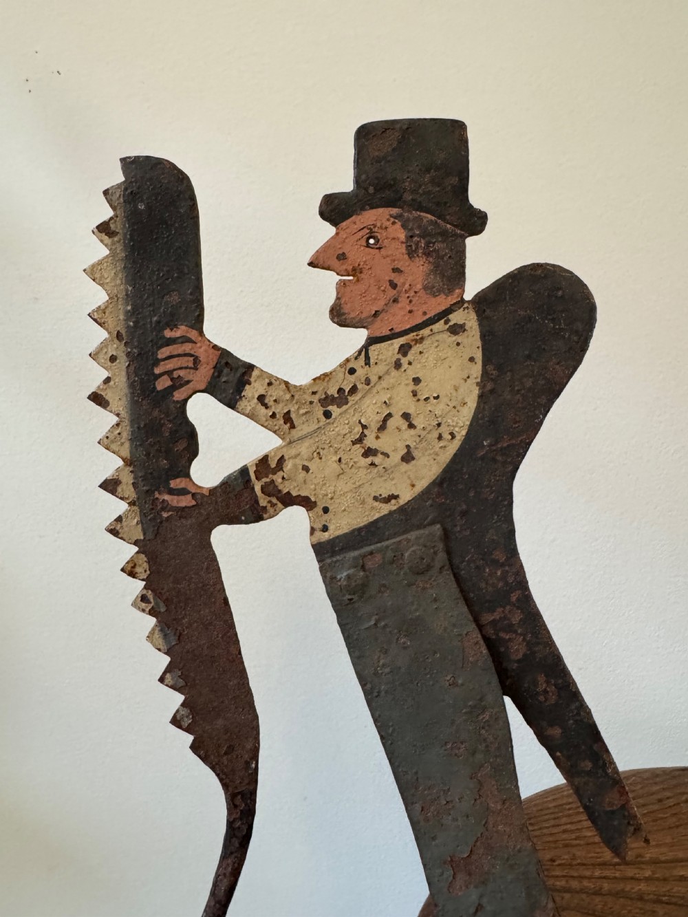 A painted metal folk art figure depicting a sawyer wearing a top hat and holding a serrated saw with aged paint loss and oxidised patina. View VIII
