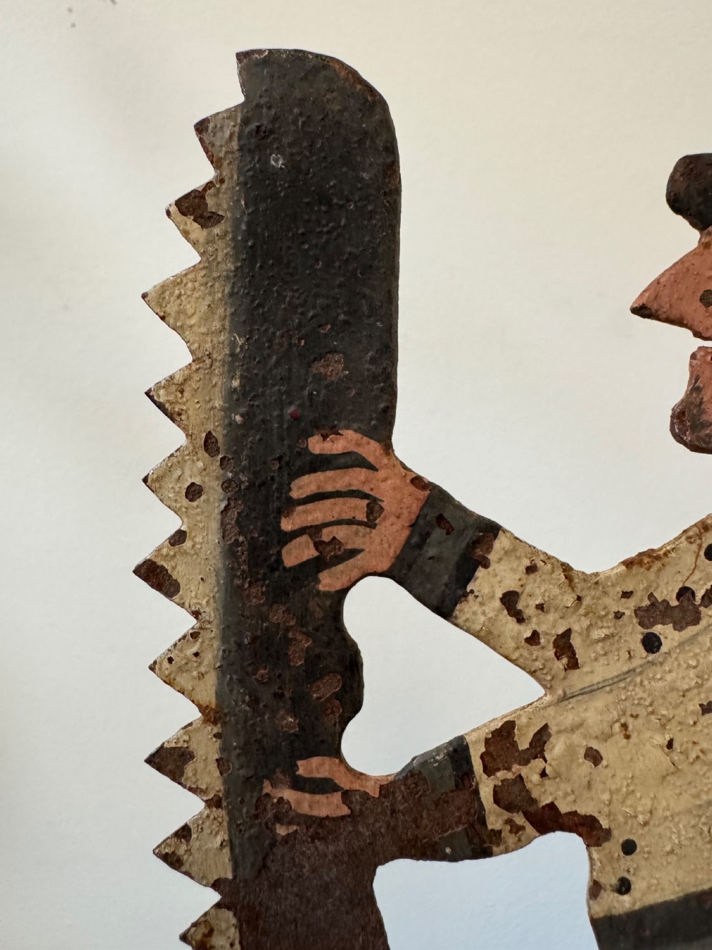 A painted metal folk art figure depicting a sawyer wearing a top hat and holding a serrated saw with aged paint loss and oxidised patina. View X