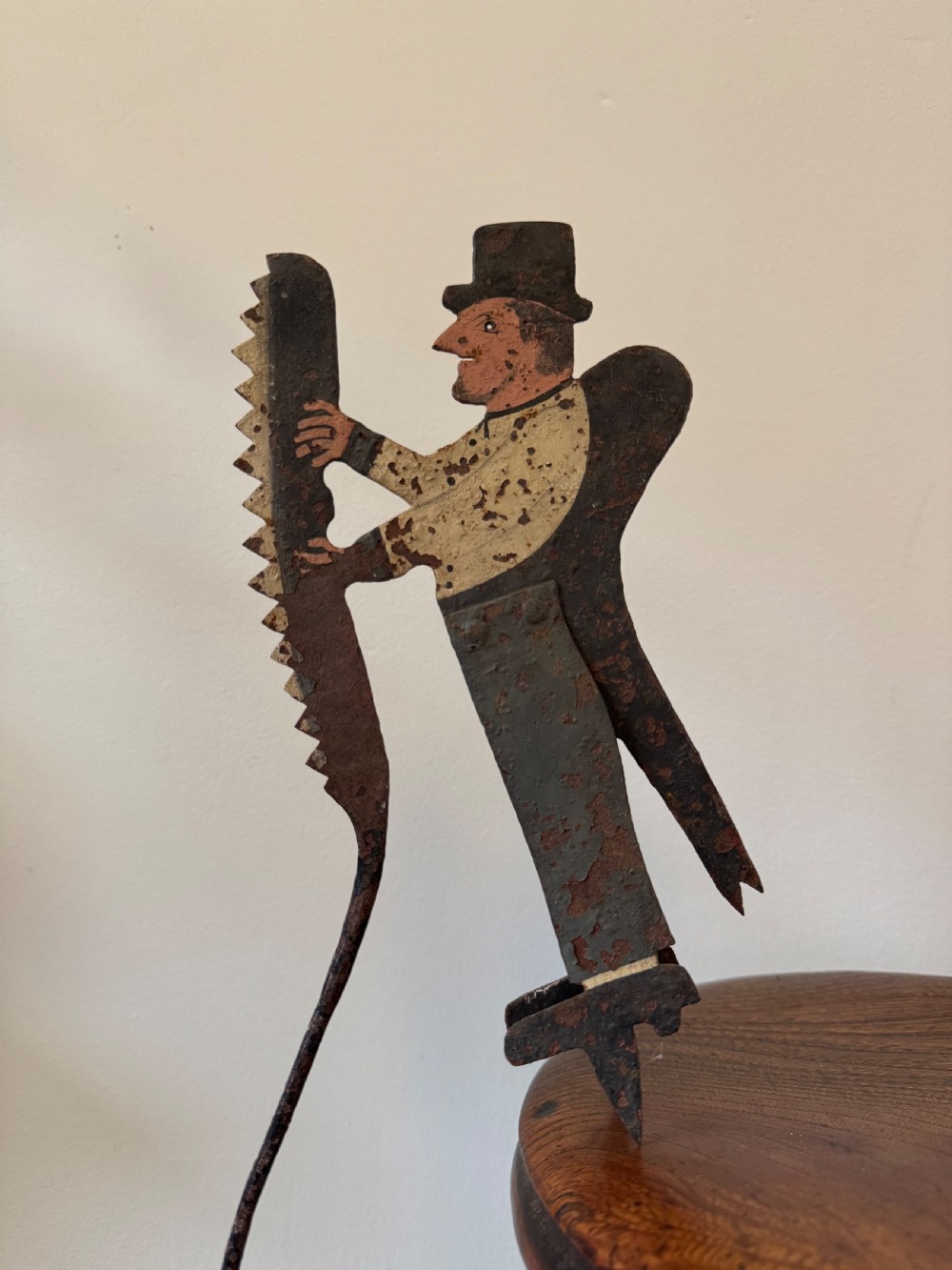 A painted metal folk art figure depicting a sawyer wearing a top hat and holding a serrated saw with aged paint loss and oxidised patina. View XI