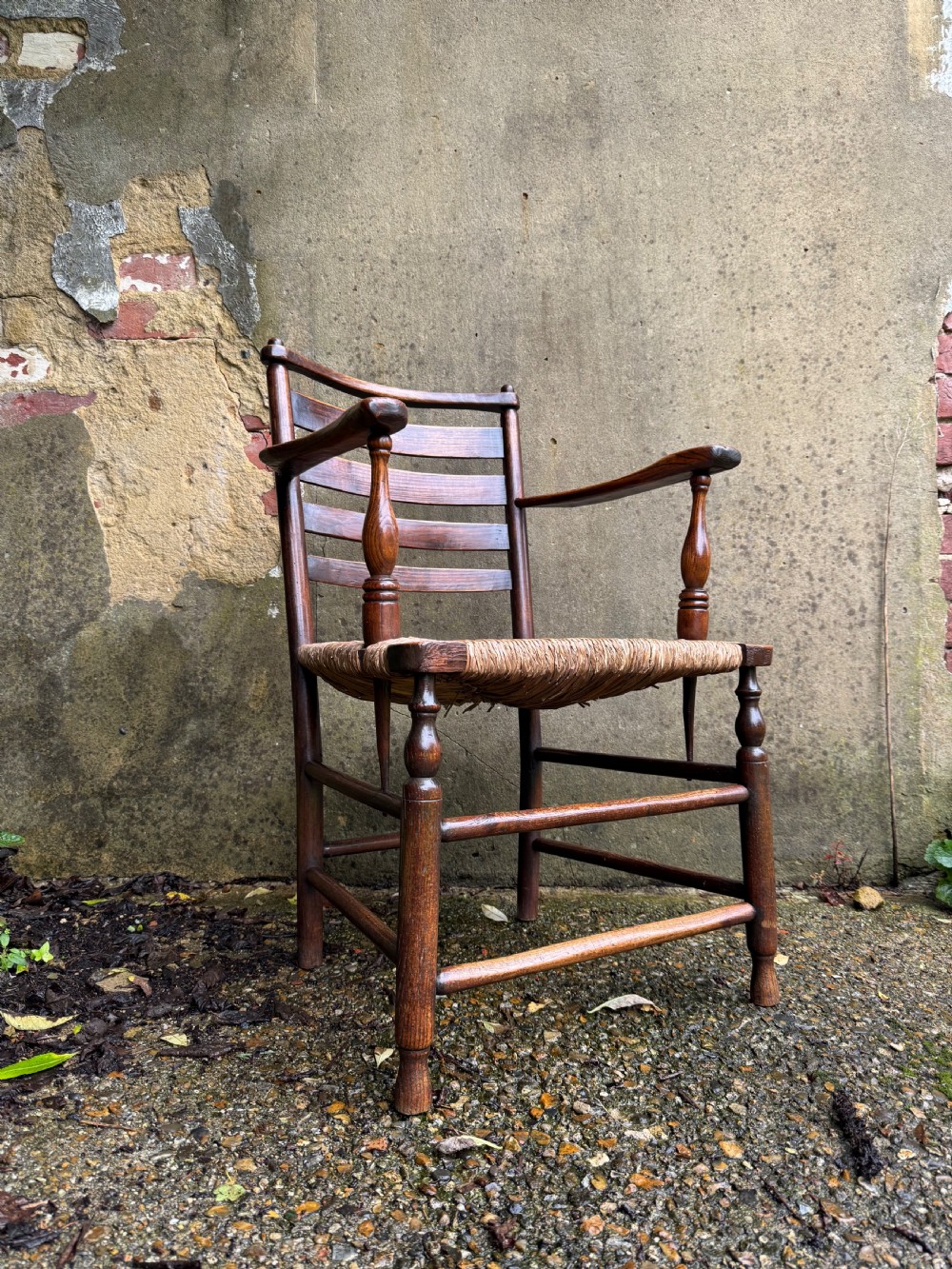 An antique dark wood Sussex armchair featuring a slatted backrest, turned front legs and stretchers, shaped armrests, and a hand-woven rush seat. View II