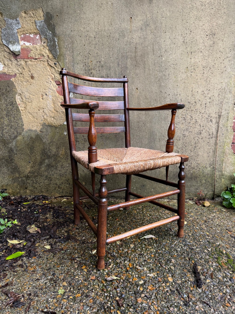 An antique dark wood Sussex armchair featuring a slatted backrest, turned front legs and stretchers, shaped armrests, and a hand-woven rush seat. View III