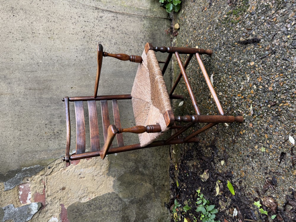 An antique dark wood Sussex armchair featuring a slatted backrest, turned front legs and stretchers, shaped armrests, and a hand-woven rush seat. View IV