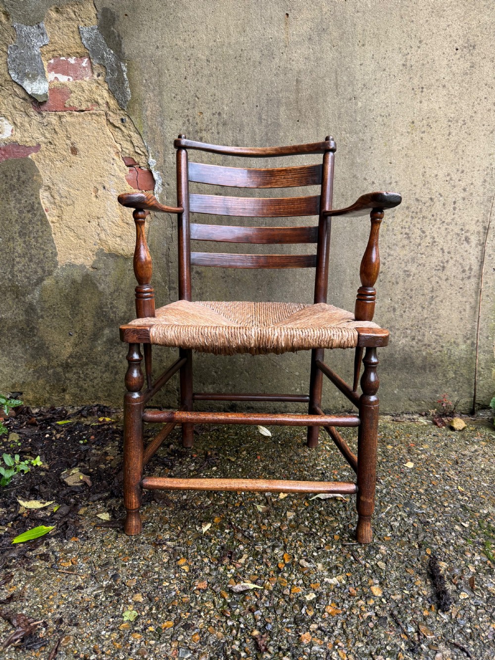 An antique dark wood Sussex armchair featuring a slatted backrest, turned front legs and stretchers, shaped armrests, and a hand-woven rush seat. View V
