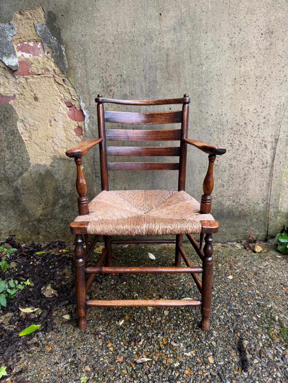 An antique dark wood Sussex armchair featuring a slatted backrest, turned front legs and stretchers, shaped armrests, and a hand-woven rush seat. View VI