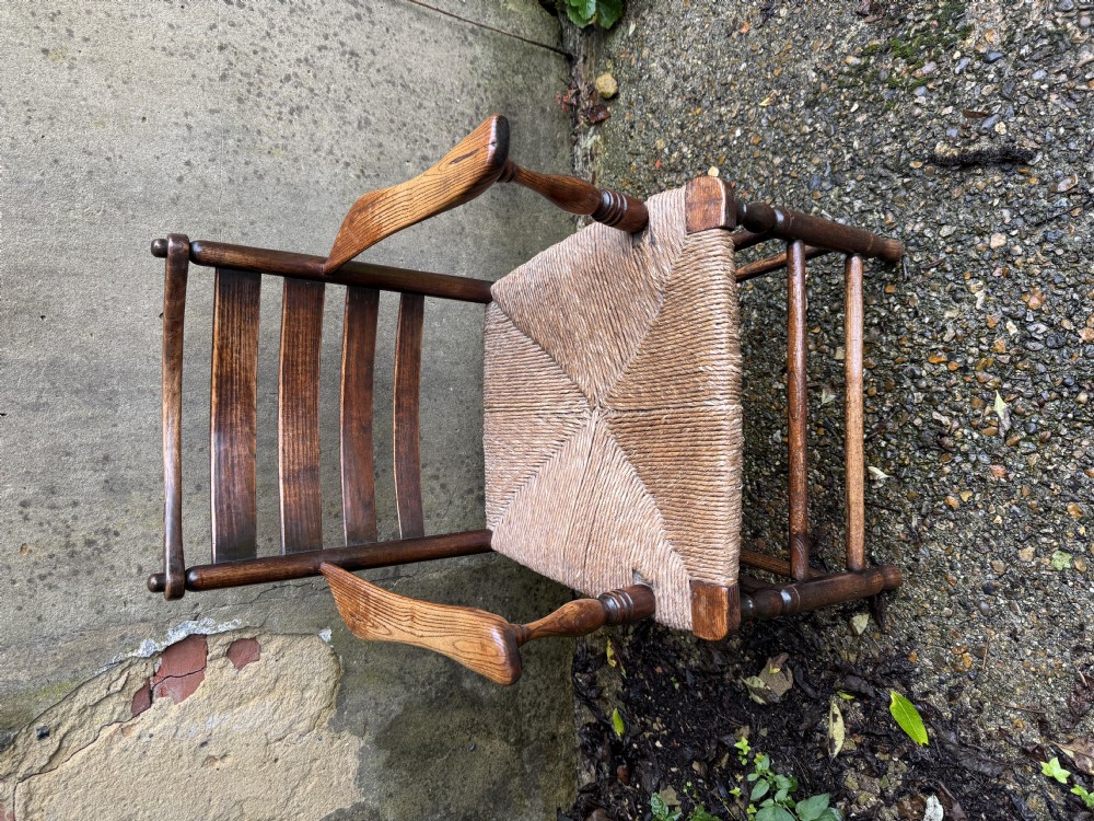 An antique dark wood Sussex armchair featuring a slatted backrest, turned front legs and stretchers, shaped armrests, and a hand-woven rush seat. View VII