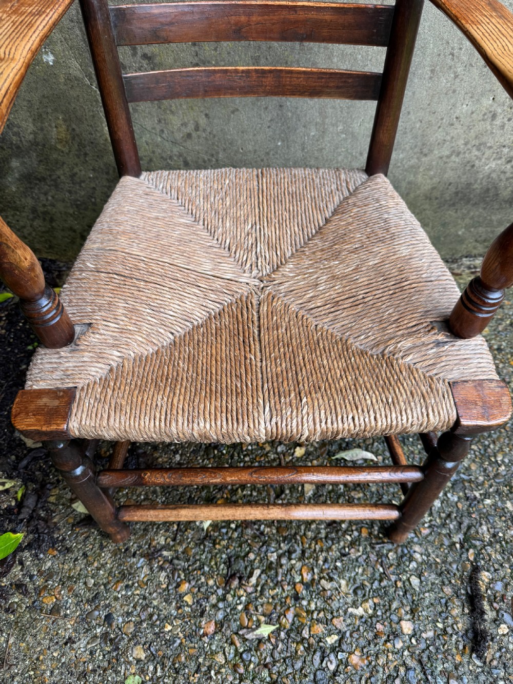 An antique dark wood Sussex armchair featuring a slatted backrest, turned front legs and stretchers, shaped armrests, and a hand-woven rush seat. View VIII