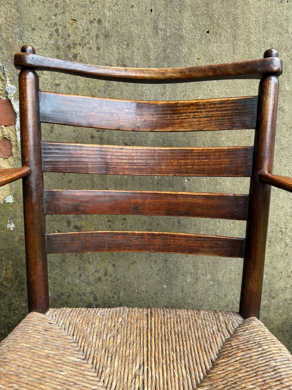 An antique dark wood Sussex armchair featuring a slatted backrest, turned front legs and stretchers, shaped armrests, and a hand-woven rush seat. View IX