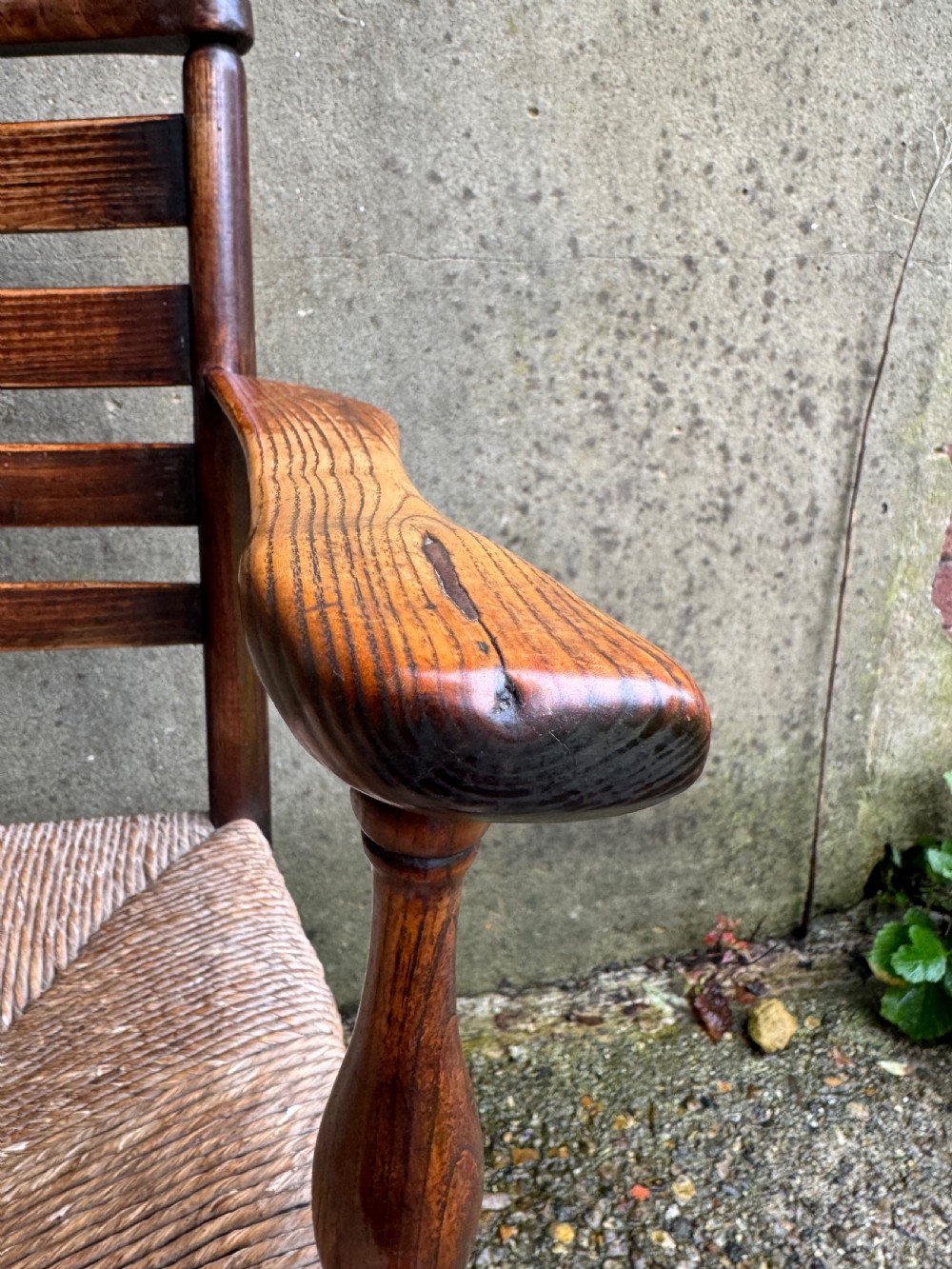 An antique dark wood Sussex armchair featuring a slatted backrest, turned front legs and stretchers, shaped armrests, and a hand-woven rush seat. View X