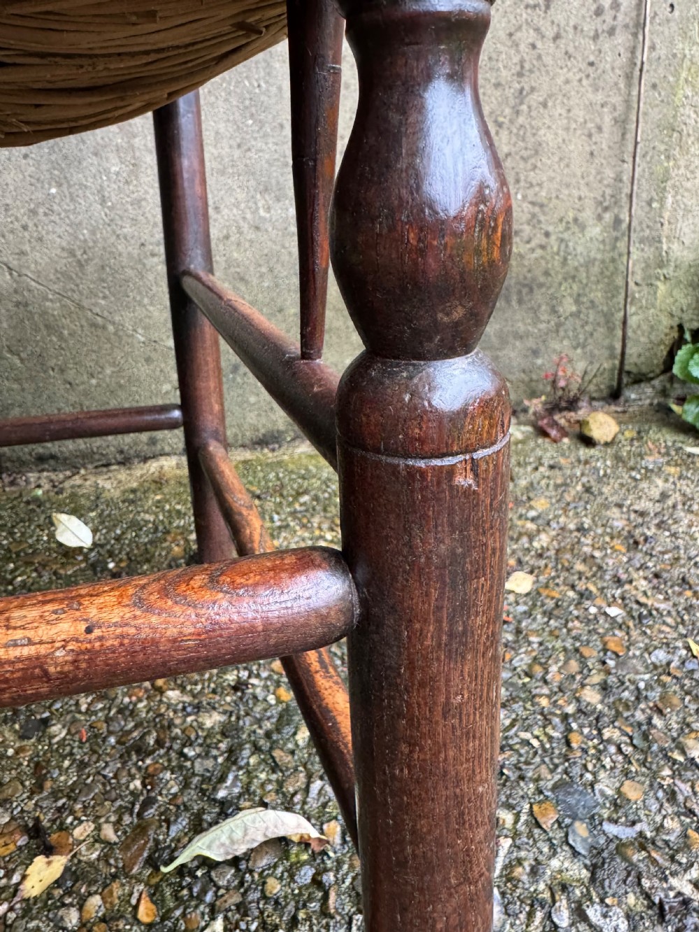 An antique dark wood Sussex armchair featuring a slatted backrest, turned front legs and stretchers, shaped armrests, and a hand-woven rush seat. View XII