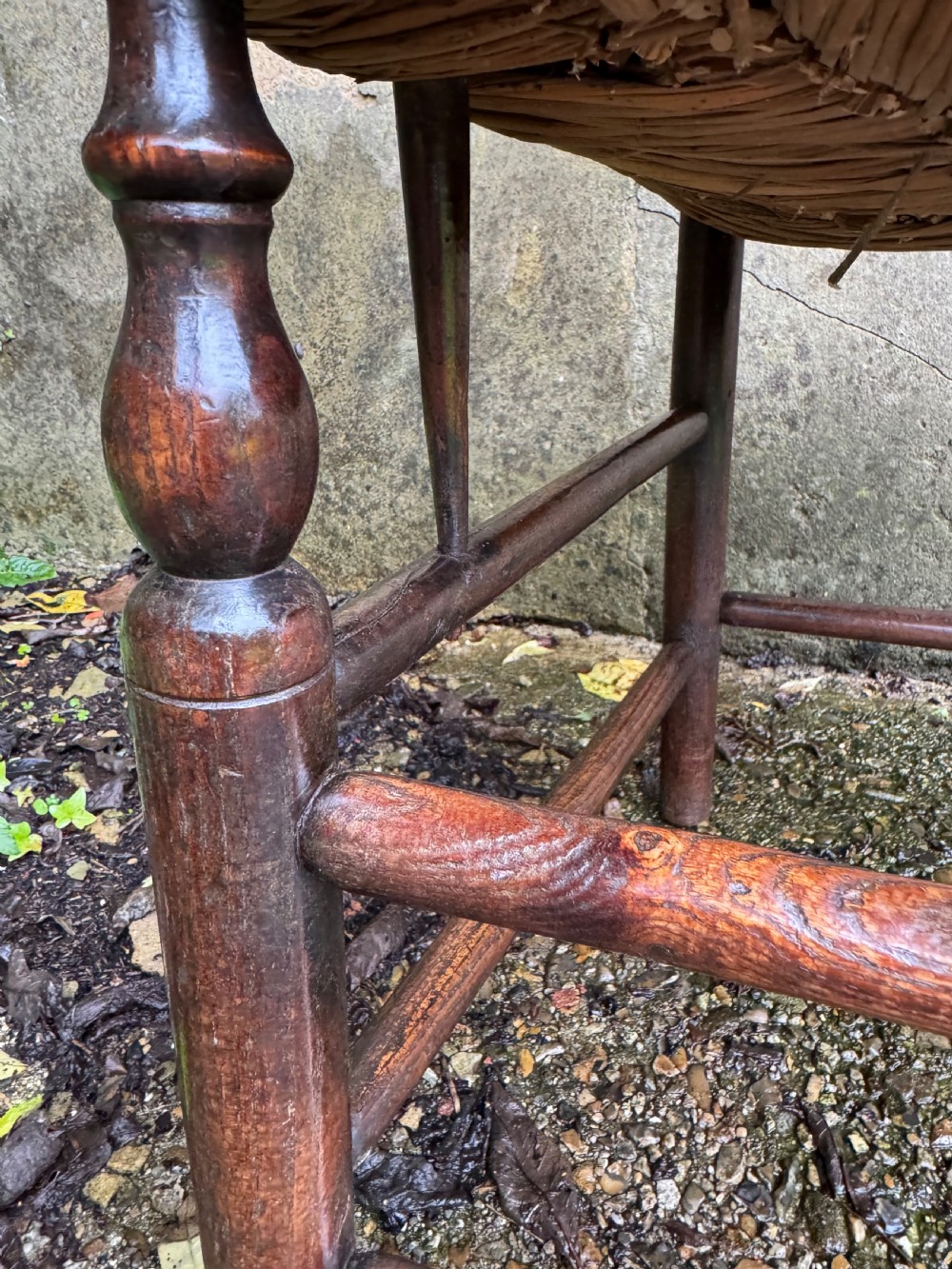 An antique dark wood Sussex armchair featuring a slatted backrest, turned front legs and stretchers, shaped armrests, and a hand-woven rush seat. View XIII