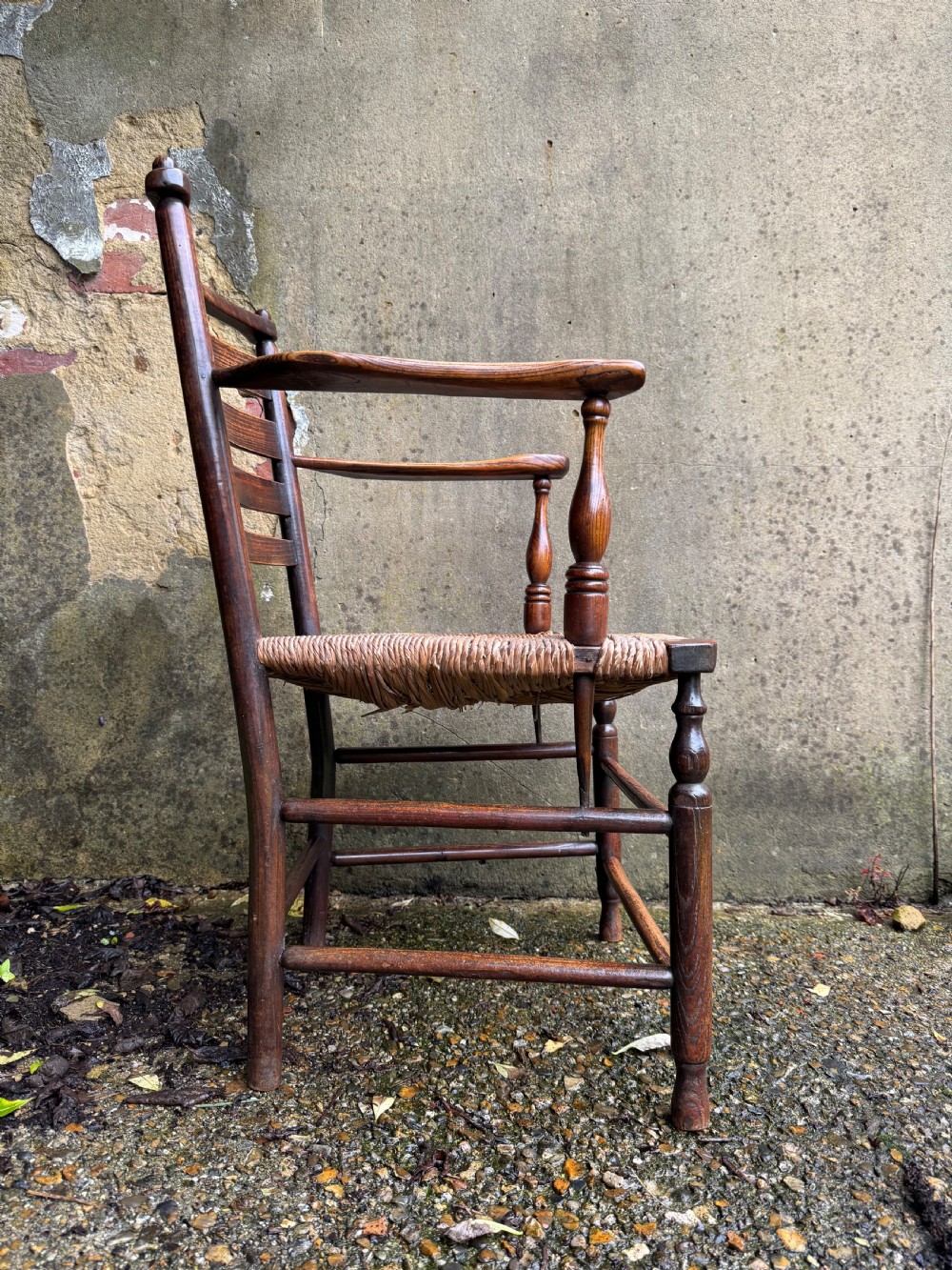 An antique dark wood Sussex armchair featuring a slatted backrest, turned front legs and stretchers, shaped armrests, and a hand-woven rush seat. View XV
