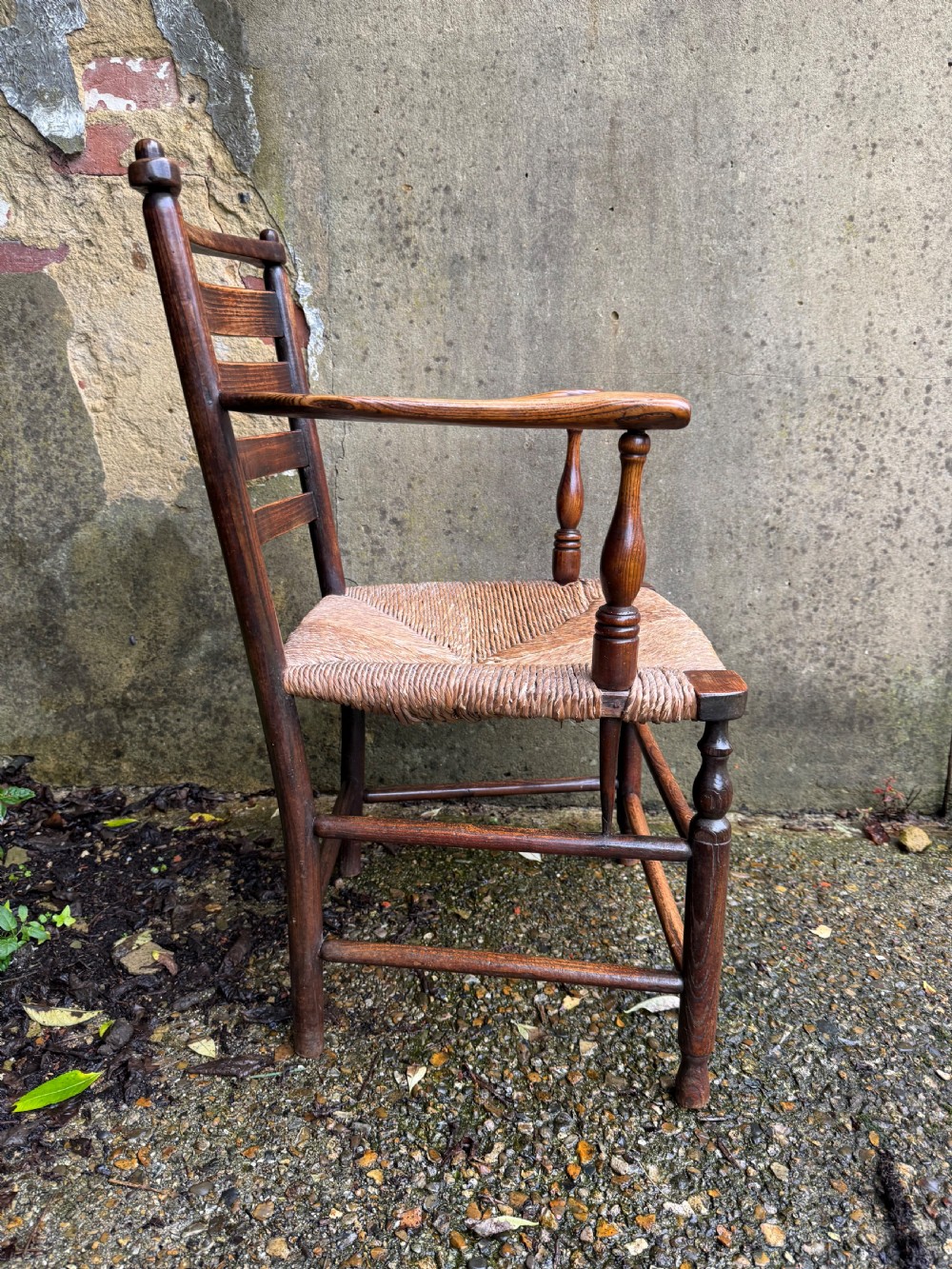 An antique dark wood Sussex armchair featuring a slatted backrest, turned front legs and stretchers, shaped armrests, and a hand-woven rush seat. View XVI