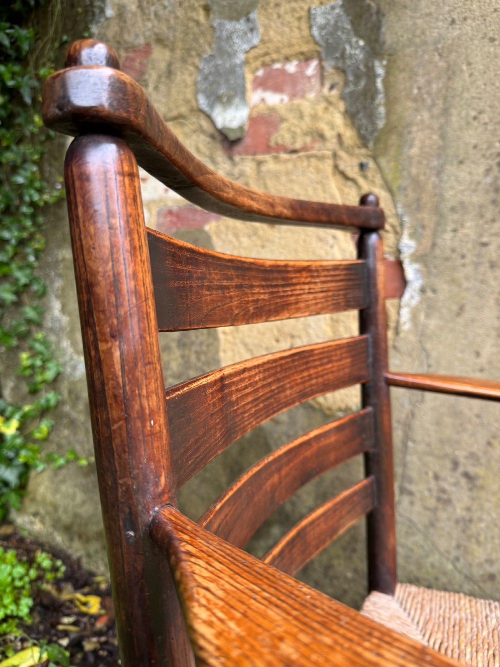 An antique dark wood Sussex armchair featuring a slatted backrest, turned front legs and stretchers, shaped armrests, and a hand-woven rush seat. View XVIII