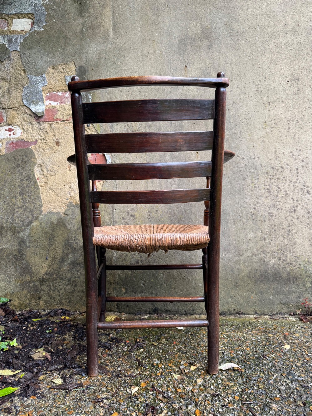 An antique dark wood Sussex armchair featuring a slatted backrest, turned front legs and stretchers, shaped armrests, and a hand-woven rush seat. View XIX