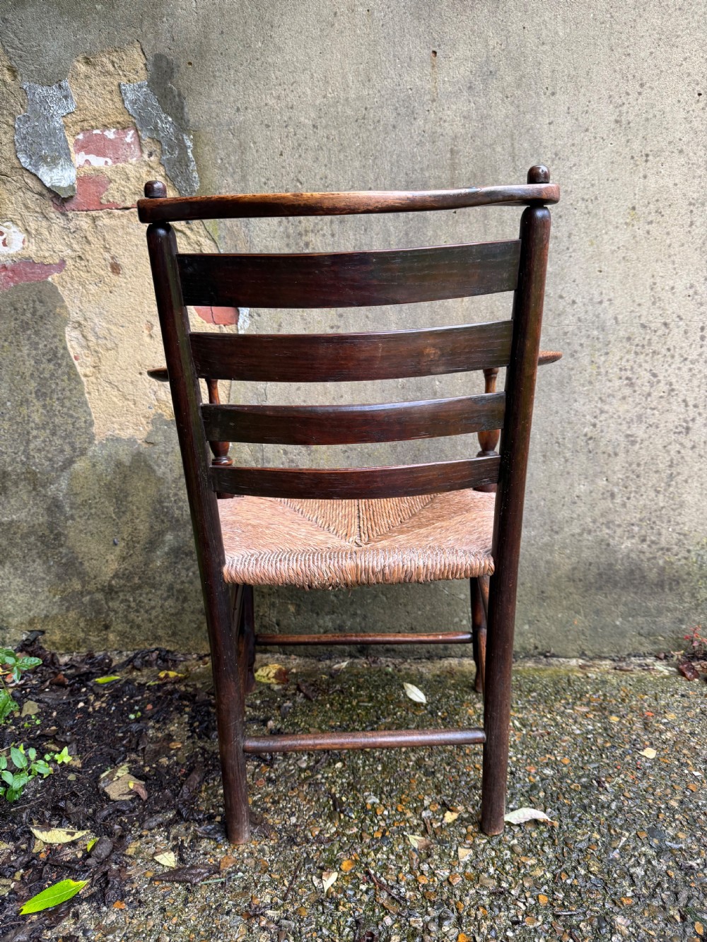 An antique dark wood Sussex armchair featuring a slatted backrest, turned front legs and stretchers, shaped armrests, and a hand-woven rush seat. View XX