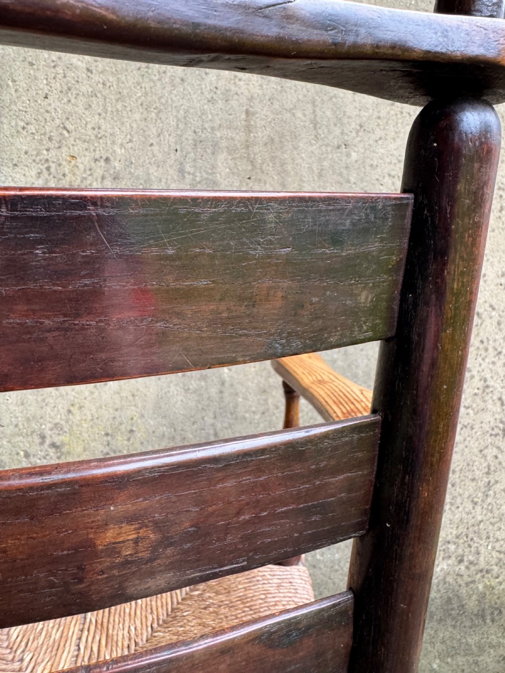 An antique dark wood Sussex armchair featuring a slatted backrest, turned front legs and stretchers, shaped armrests, and a hand-woven rush seat. View XXI