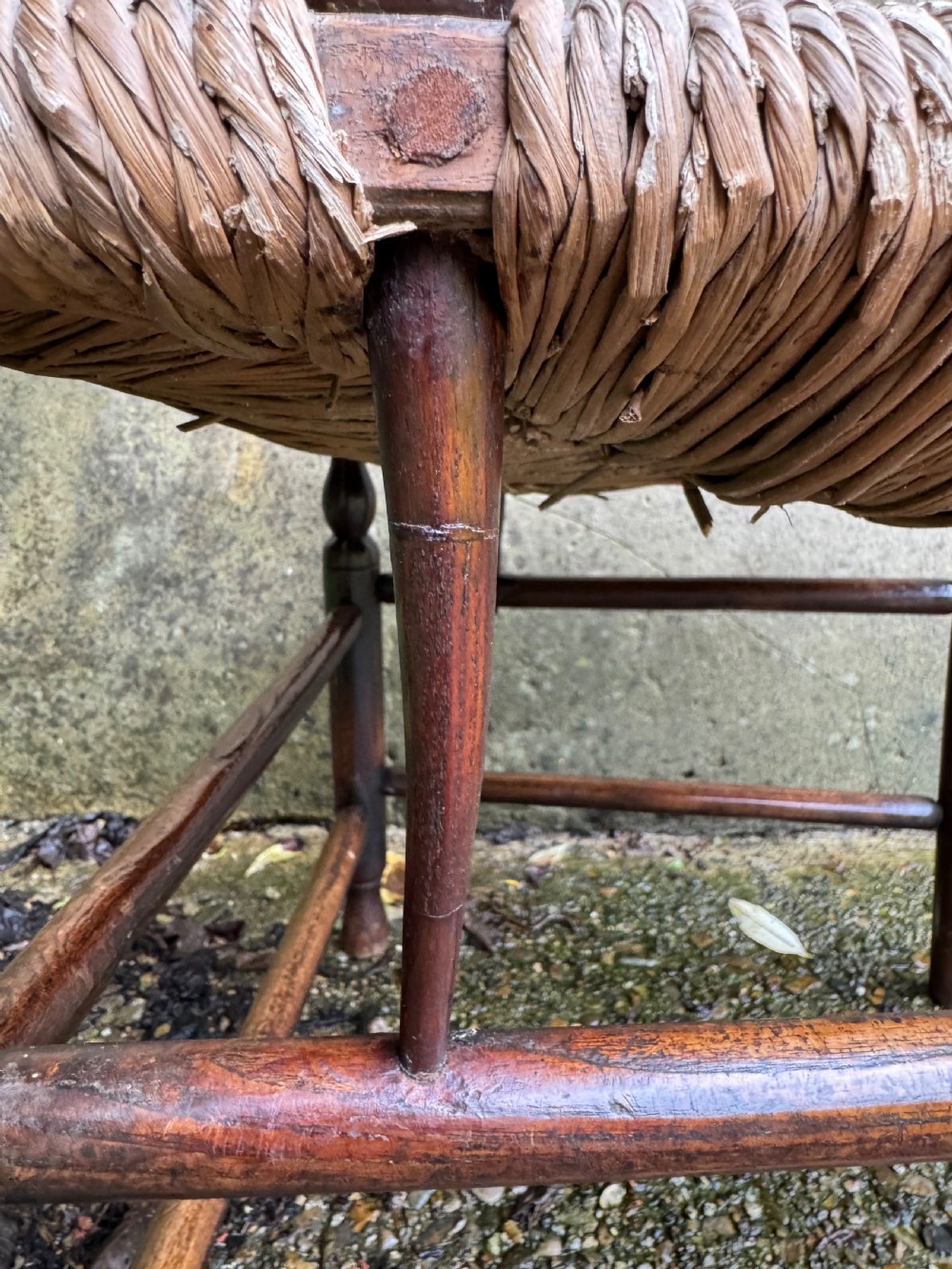 An antique dark wood Sussex armchair featuring a slatted backrest, turned front legs and stretchers, shaped armrests, and a hand-woven rush seat. View XXII