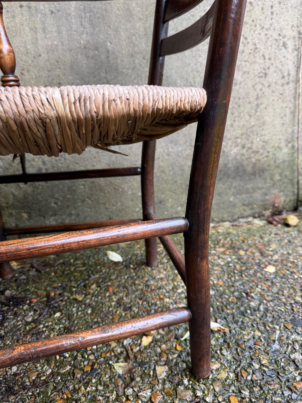 An antique dark wood Sussex armchair featuring a slatted backrest, turned front legs and stretchers, shaped armrests, and a hand-woven rush seat. View XXIII