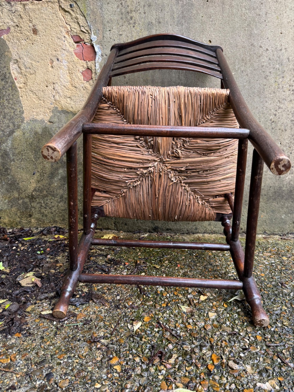 An antique dark wood Sussex armchair featuring a slatted backrest, turned front legs and stretchers, shaped armrests, and a hand-woven rush seat. View XXIV