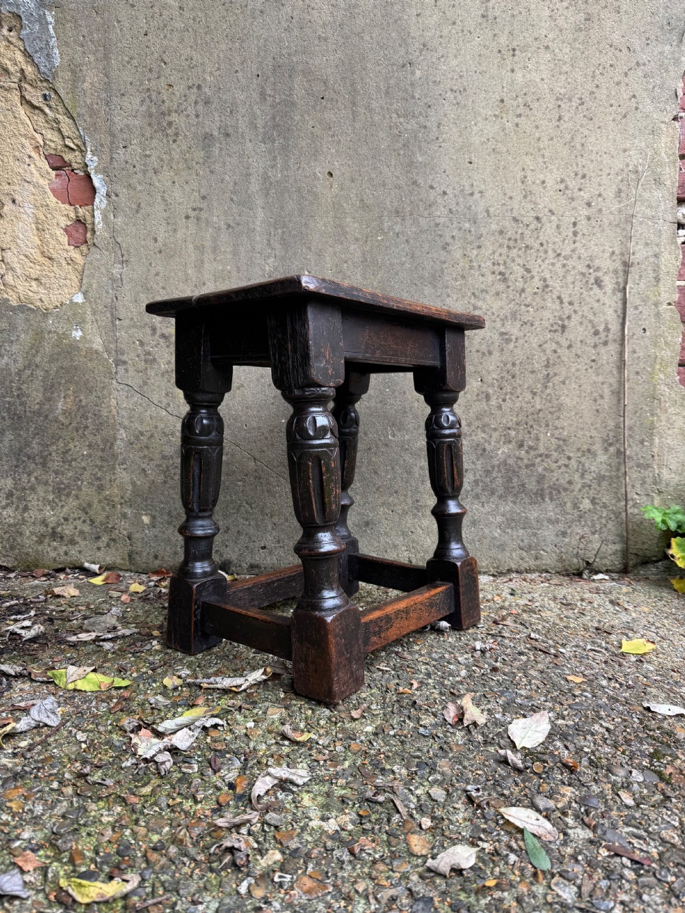 A dark oak joint stool featuring turned baluster legs, lower perimeter stretchers, and a flat rectangular top.