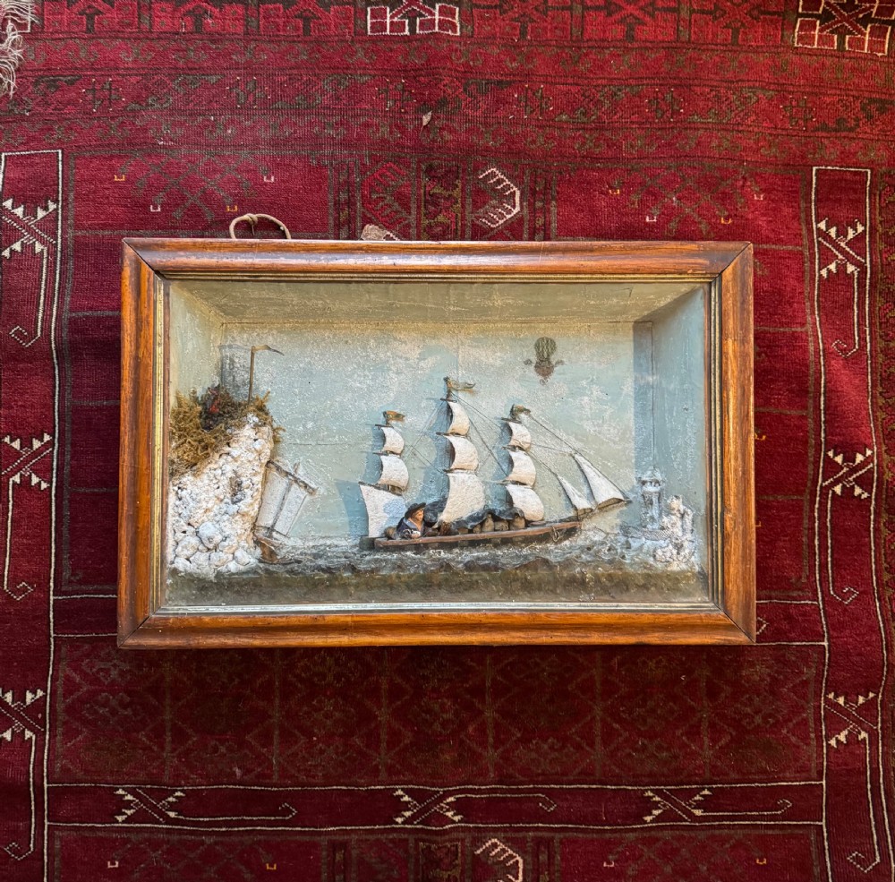 A framed shadow box diorama depicting a three-masted sailing ship on a painted plaster sea beside a rocky cliff and lighthouse. View II