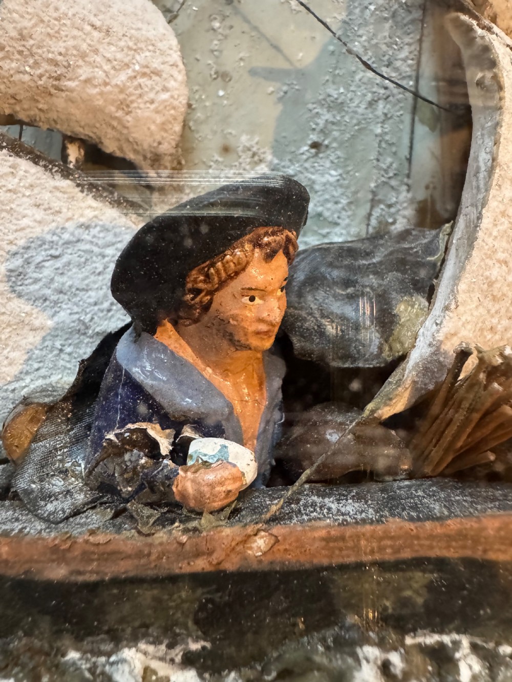 A framed shadow box diorama depicting a three-masted sailing ship on a painted plaster sea beside a rocky cliff and lighthouse. View VI