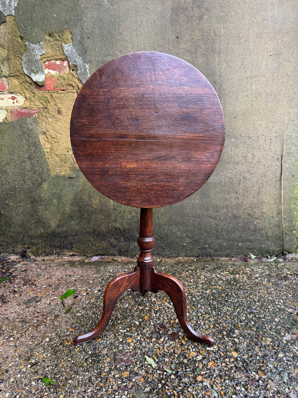 An antique dark oak circular tripod table with a turned central stem, three pad-foot legs, and a tilt-top mechanism.