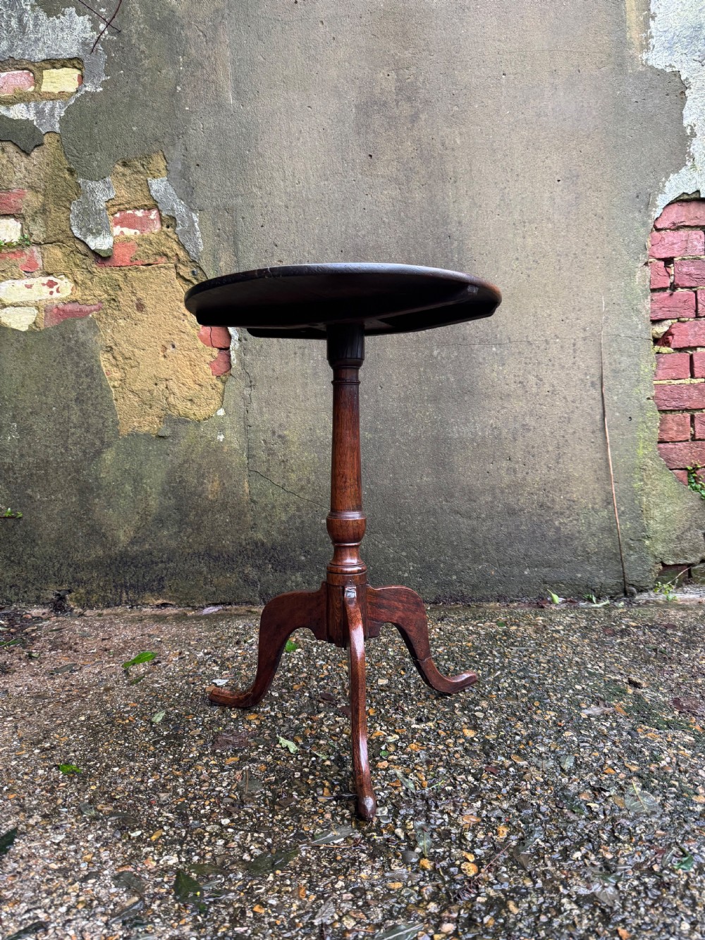 An antique dark oak circular tripod table with a turned central stem, three pad-foot legs, and a tilt-top mechanism. View II