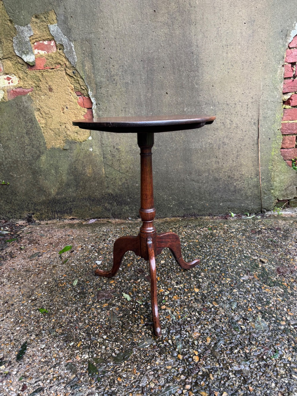 An antique dark oak circular tripod table with a turned central stem, three pad-foot legs, and a tilt-top mechanism. View III