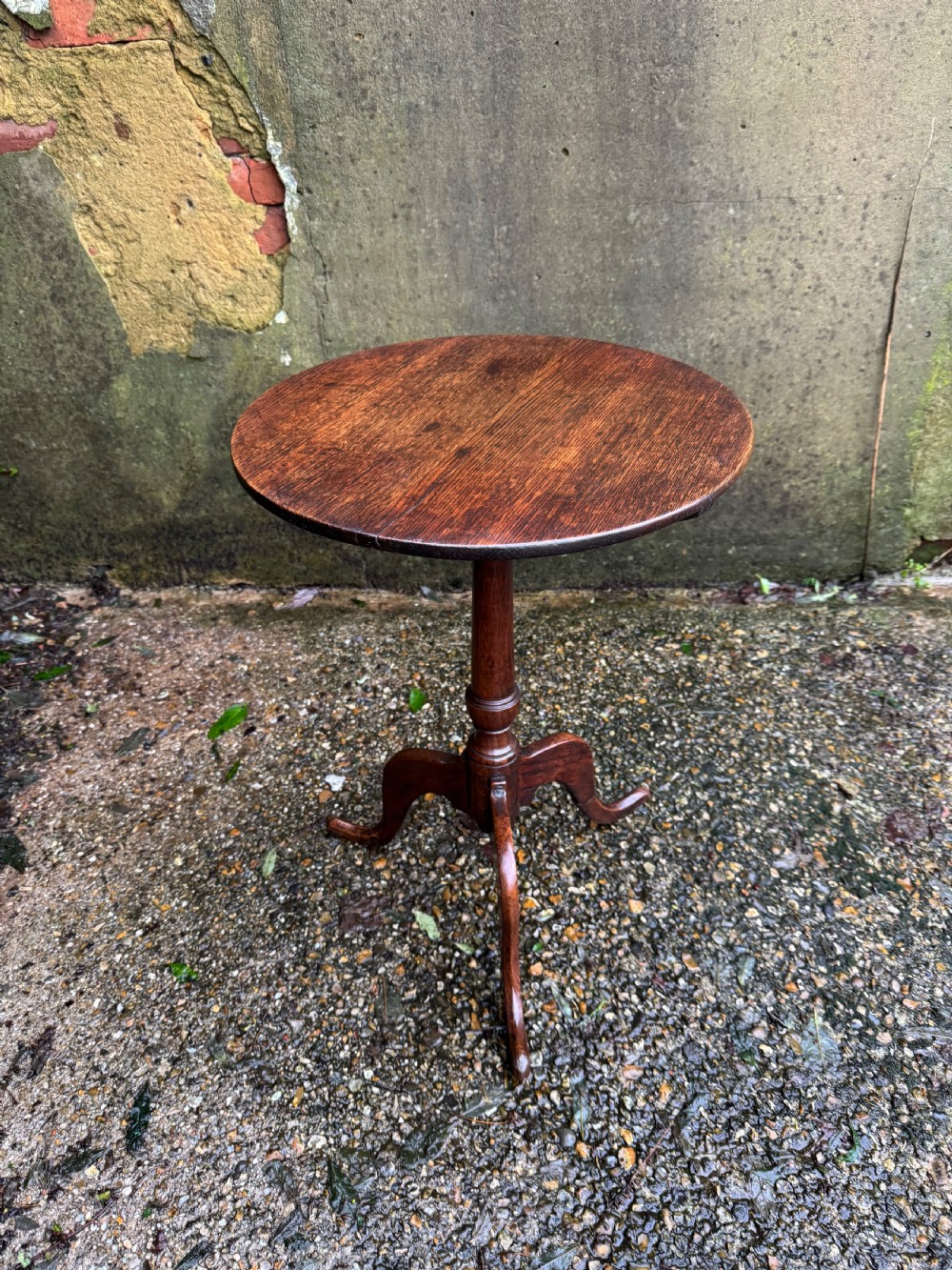 An antique dark oak circular tripod table with a turned central stem, three pad-foot legs, and a tilt-top mechanism. View IV