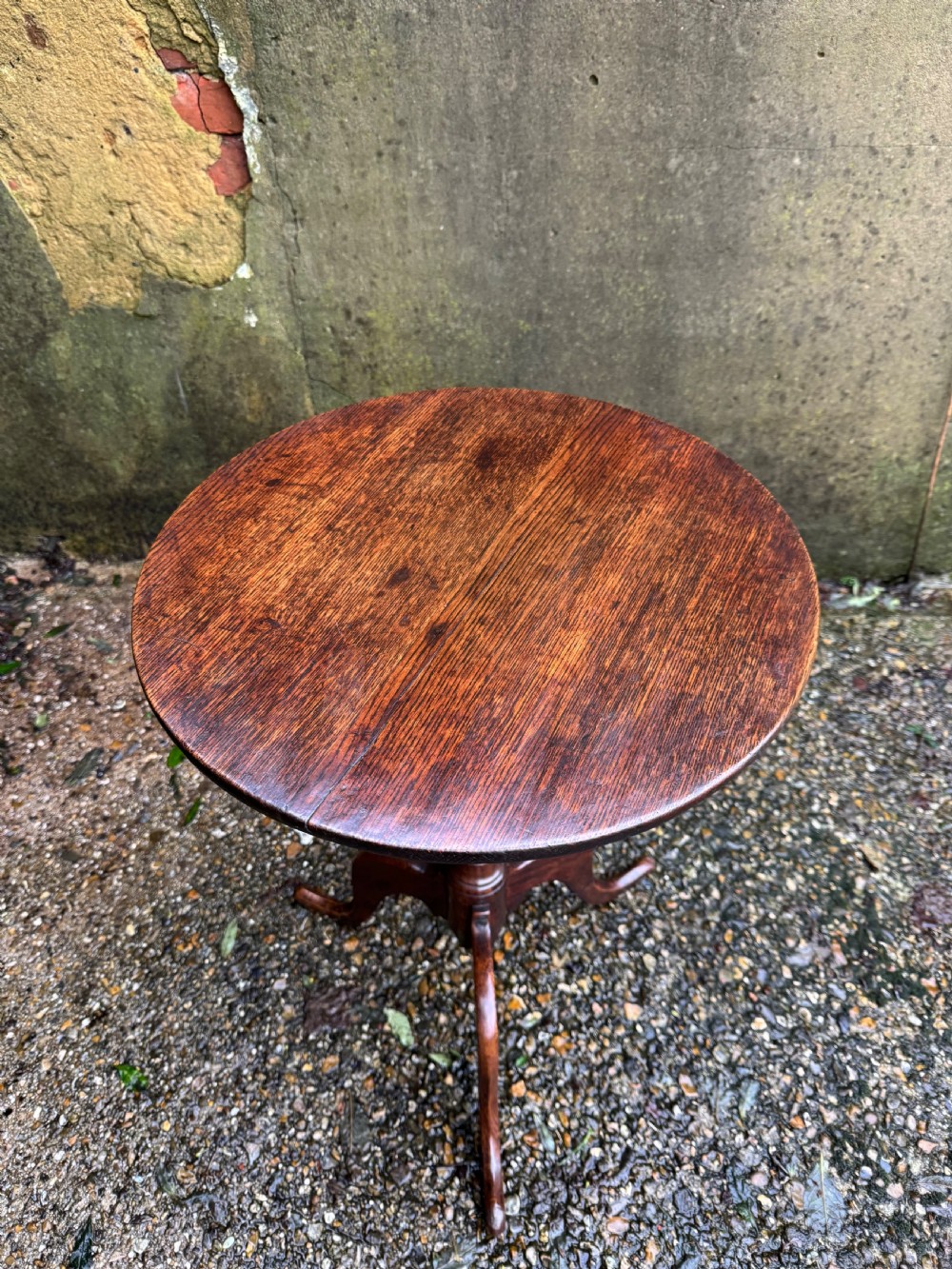 An antique dark oak circular tripod table with a turned central stem, three pad-foot legs, and a tilt-top mechanism. View V