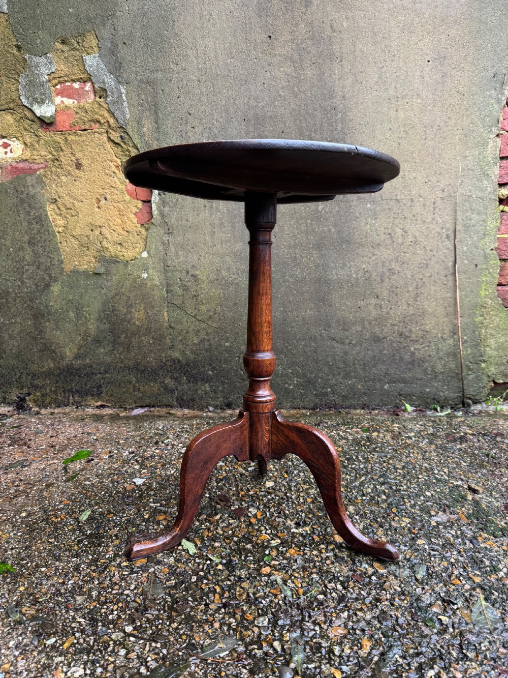 An antique dark oak circular tripod table with a turned central stem, three pad-foot legs, and a tilt-top mechanism. View VI