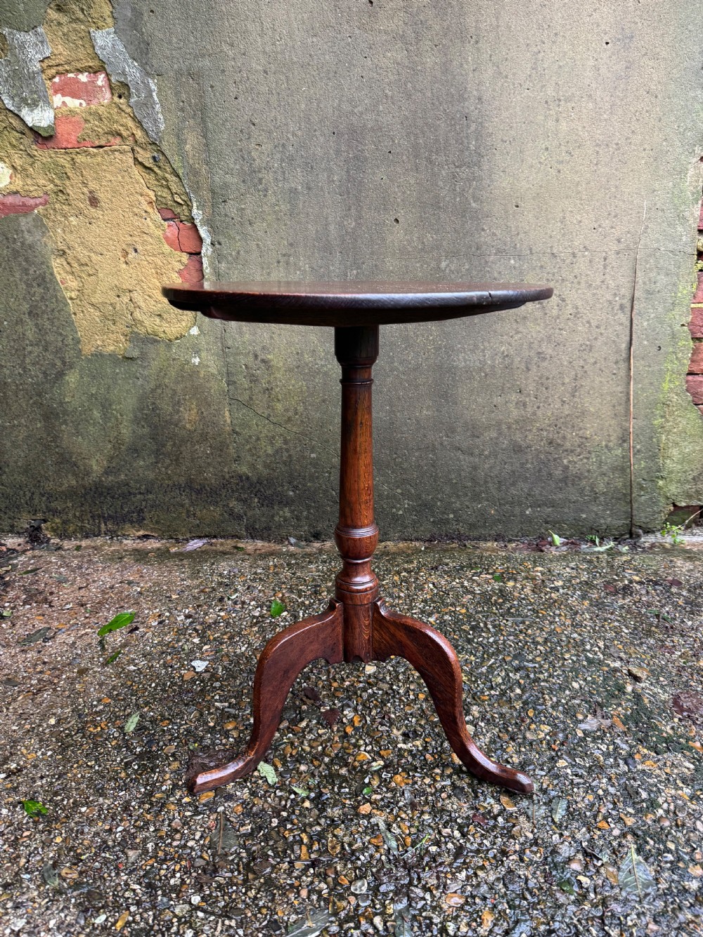 An antique dark oak circular tripod table with a turned central stem, three pad-foot legs, and a tilt-top mechanism. View VII