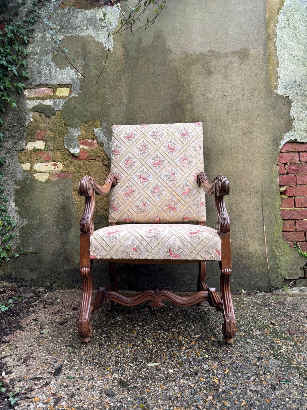 A French style carved walnut armchair featuring a tall backrest, scrolled armrests, patterned cream and pink upholstery, and intricately carved legs. View II