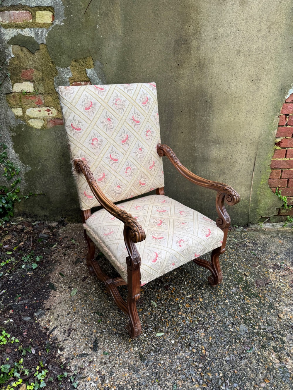 A French style carved walnut armchair featuring a tall backrest, scrolled armrests, patterned cream and pink upholstery, and intricately carved legs. View IV