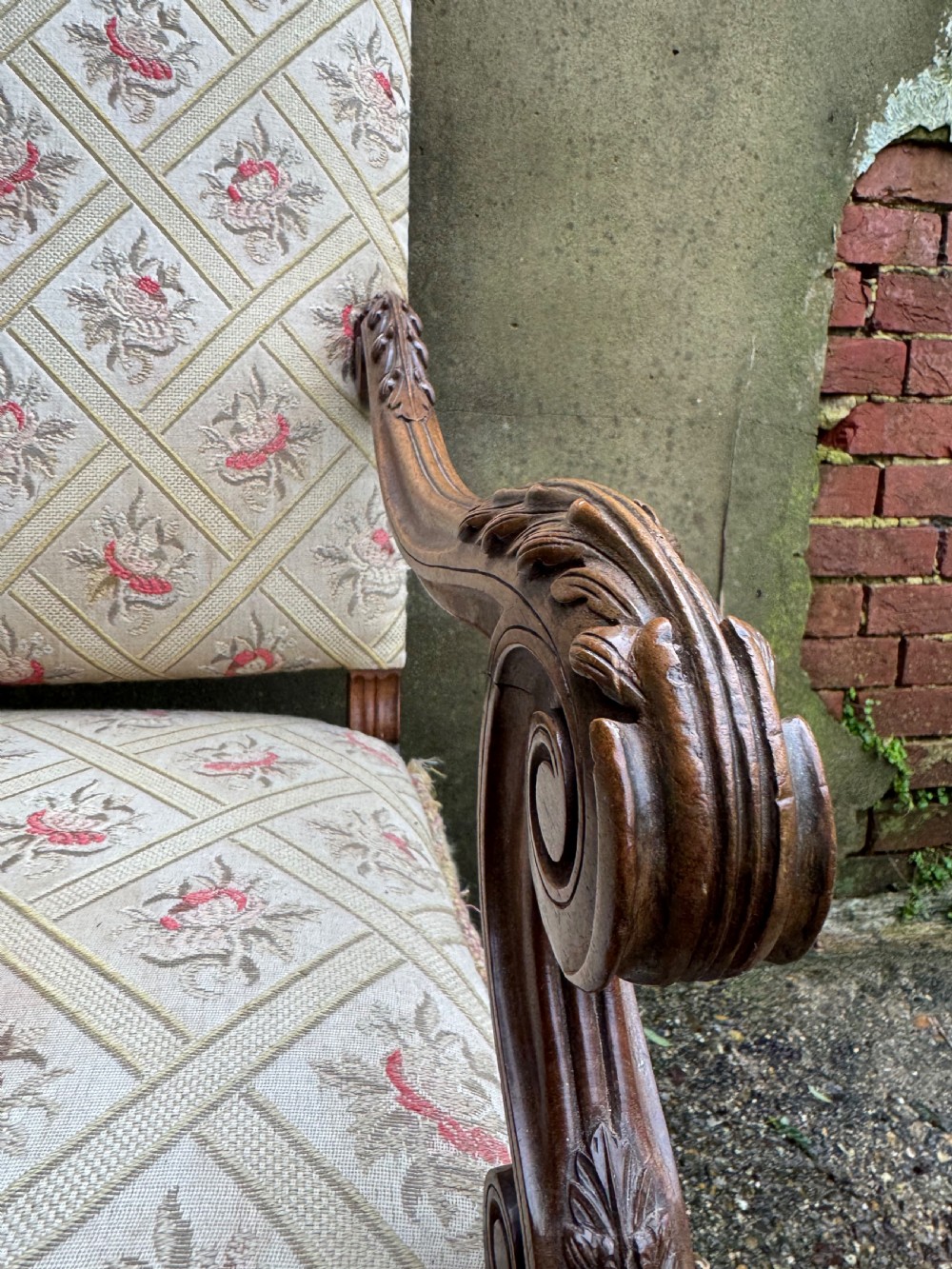 A French style carved walnut armchair featuring a tall backrest, scrolled armrests, patterned cream and pink upholstery, and intricately carved legs. View V