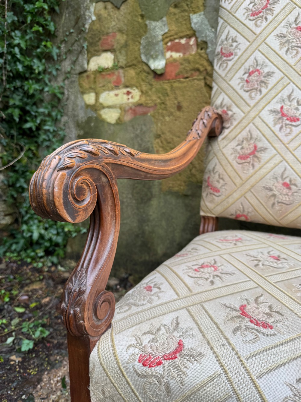A French style carved walnut armchair featuring a tall backrest, scrolled armrests, patterned cream and pink upholstery, and intricately carved legs. View VI