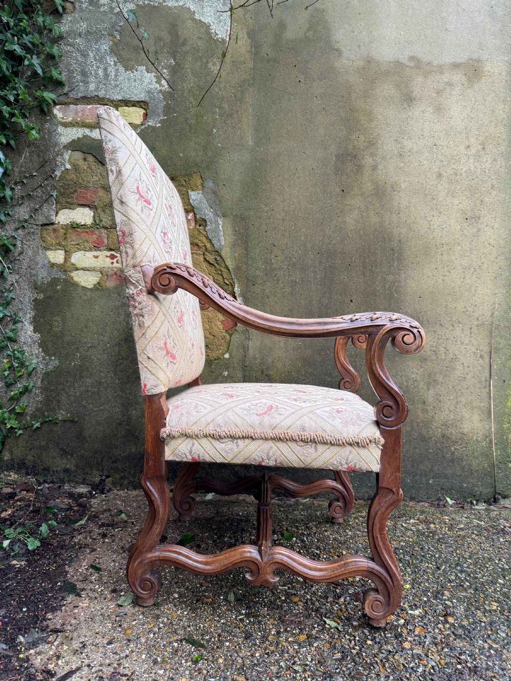 A French style carved walnut armchair featuring a tall backrest, scrolled armrests, patterned cream and pink upholstery, and intricately carved legs. View X