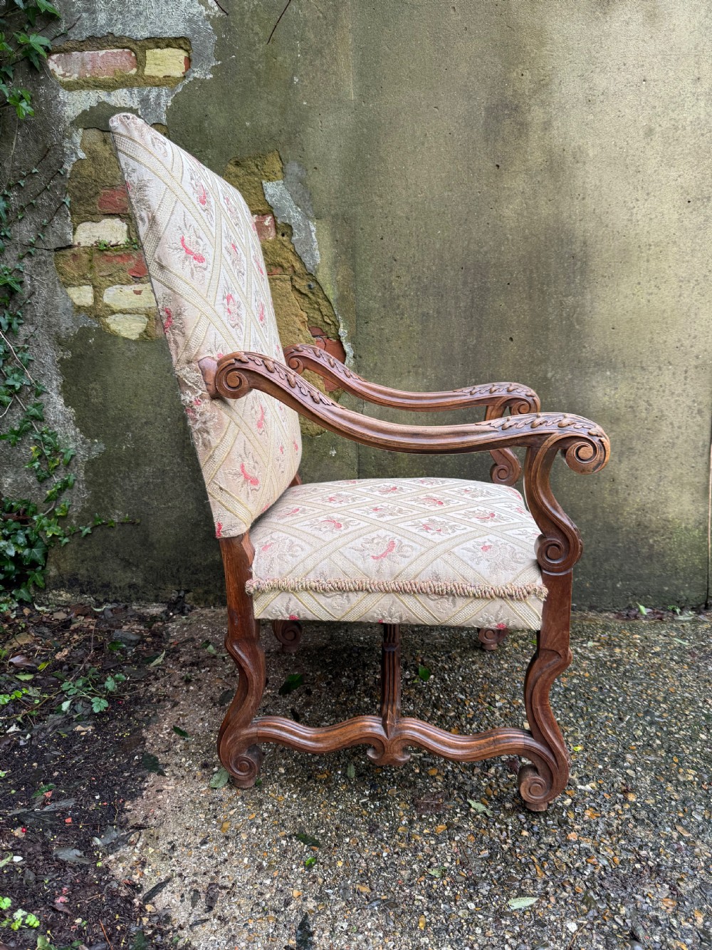 A French style carved walnut armchair featuring a tall backrest, scrolled armrests, patterned cream and pink upholstery, and intricately carved legs. View XII