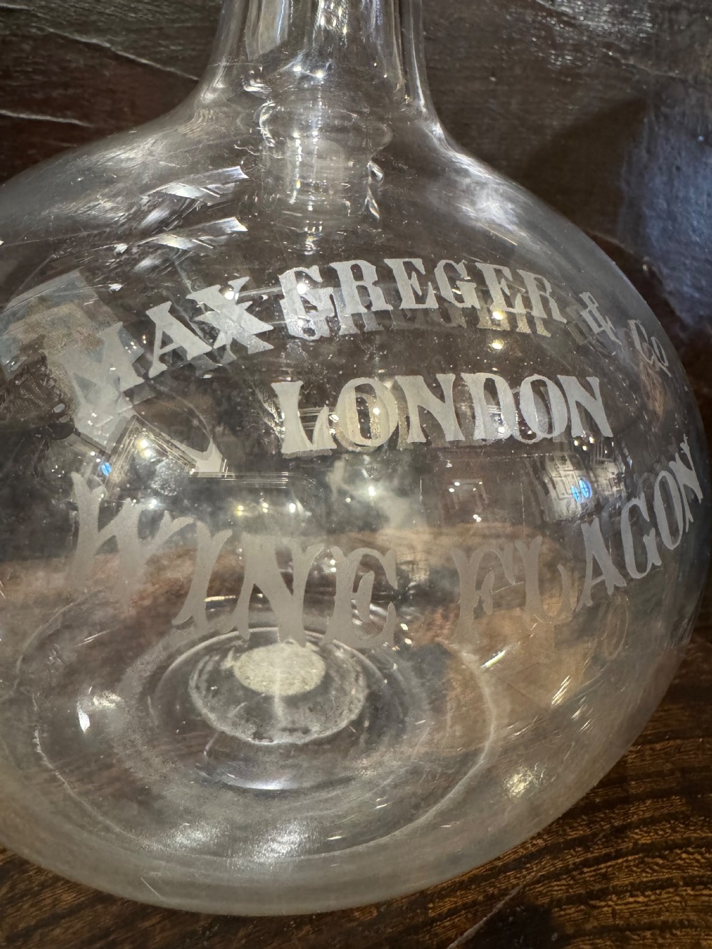 A clear bulbous glass wine flagon featuring etched lettering reading Max Greger and Co London Wine Flagon with a matching glass stopper. View IV