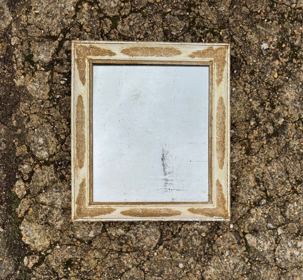A rectangular antique wall mirror featuring a distressed cream-painted timber frame decorated with gilded corner spandrels and foxed mirror glass. View II