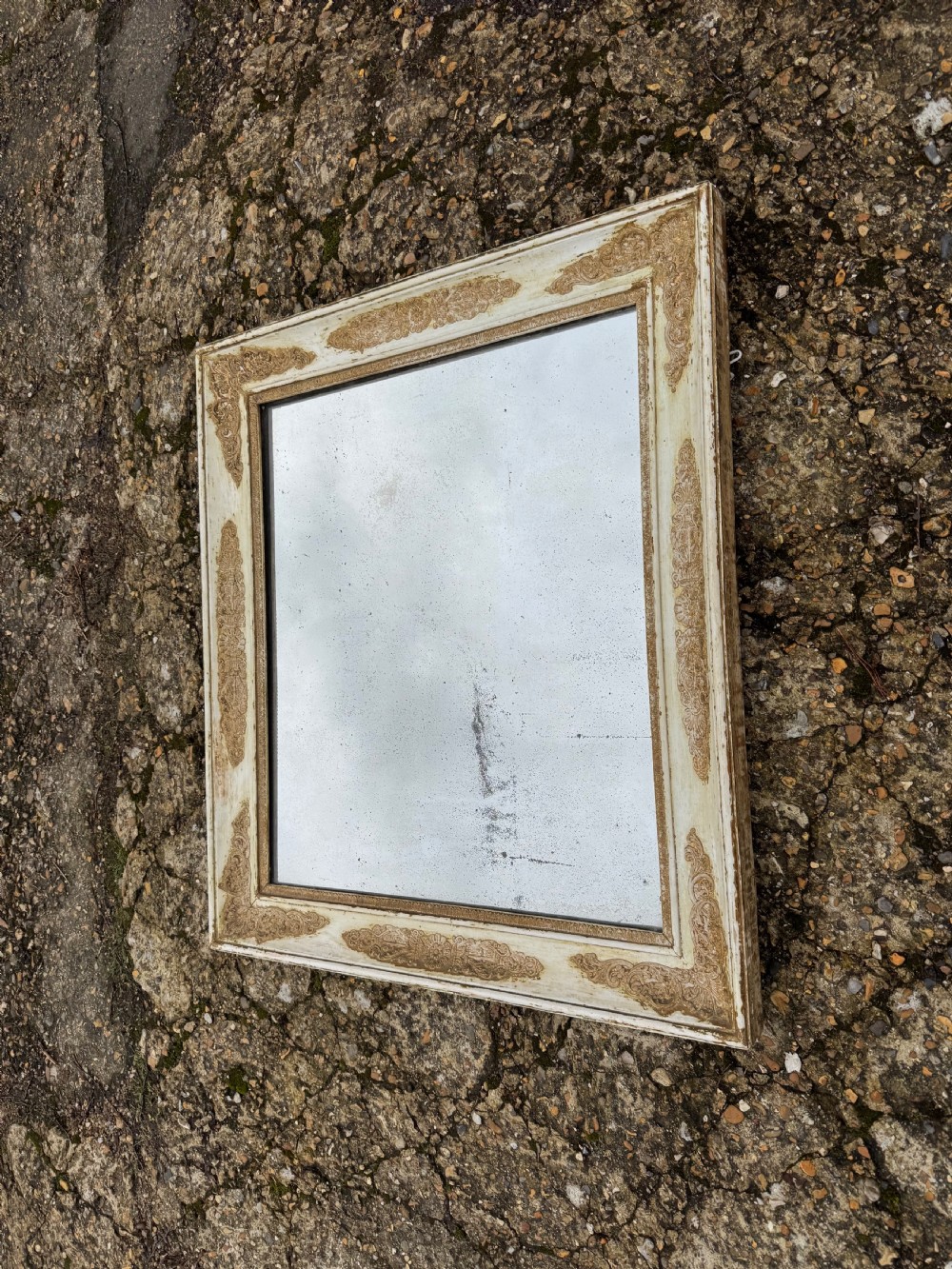 A rectangular antique wall mirror featuring a distressed cream-painted timber frame decorated with gilded corner spandrels and foxed mirror glass. View VIII