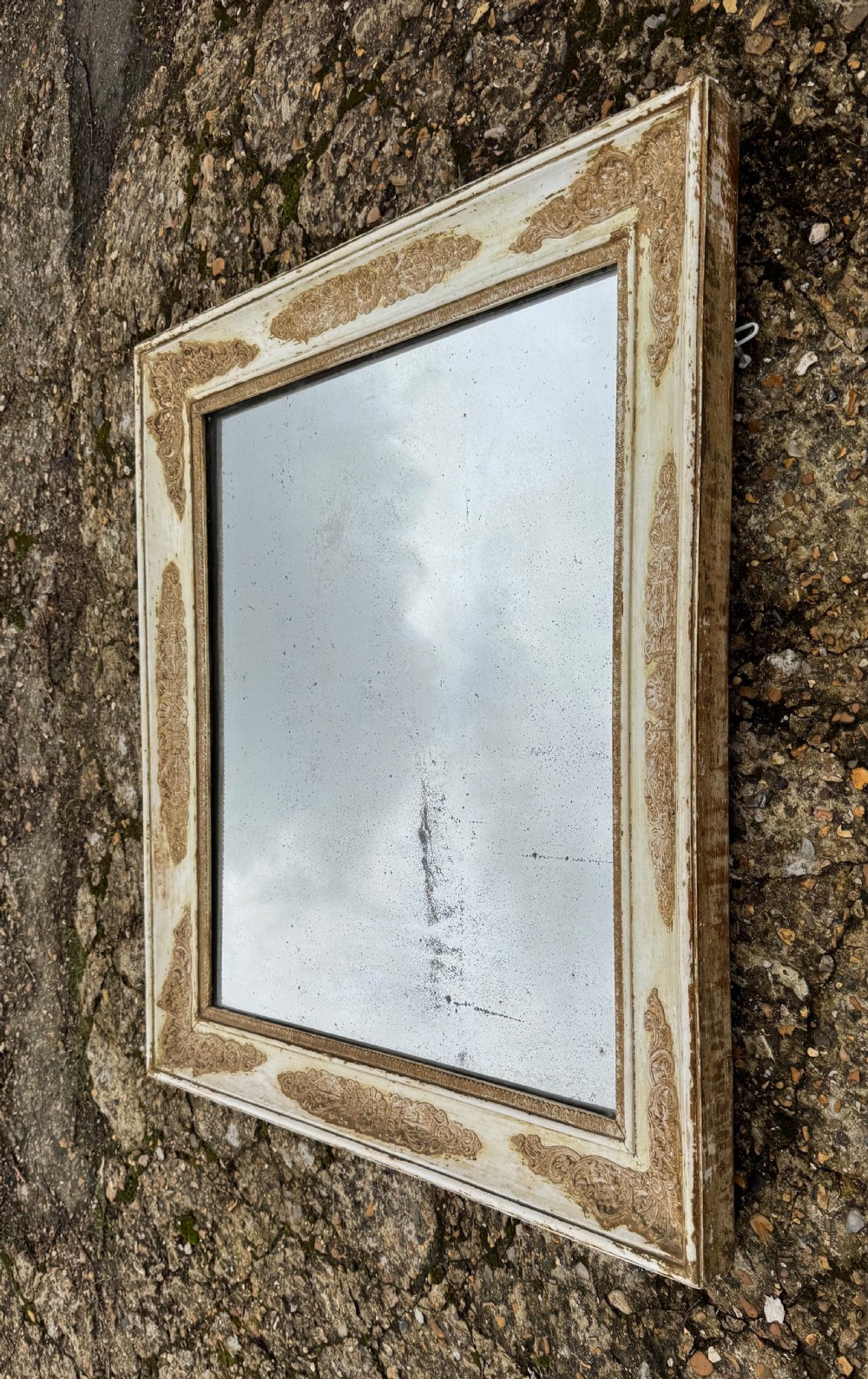 A rectangular antique wall mirror featuring a distressed cream-painted timber frame decorated with gilded corner spandrels and foxed mirror glass. View IX